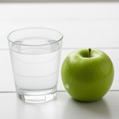 Glass of water next to a fresh apple, symbolizing healthy digestion